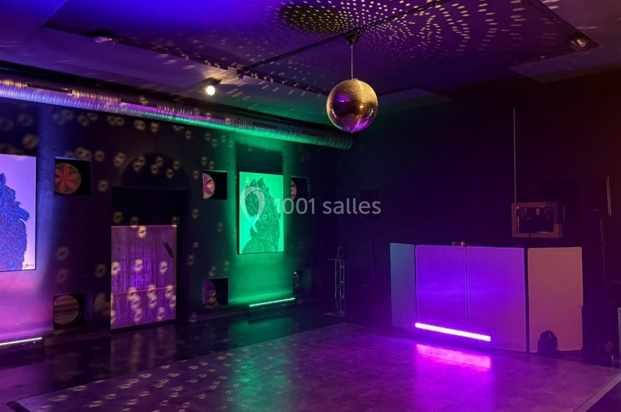 Salle sombre avec une piste de danse éclairée par une boule à facettes et des lumières colorées, décorée de tableaux.