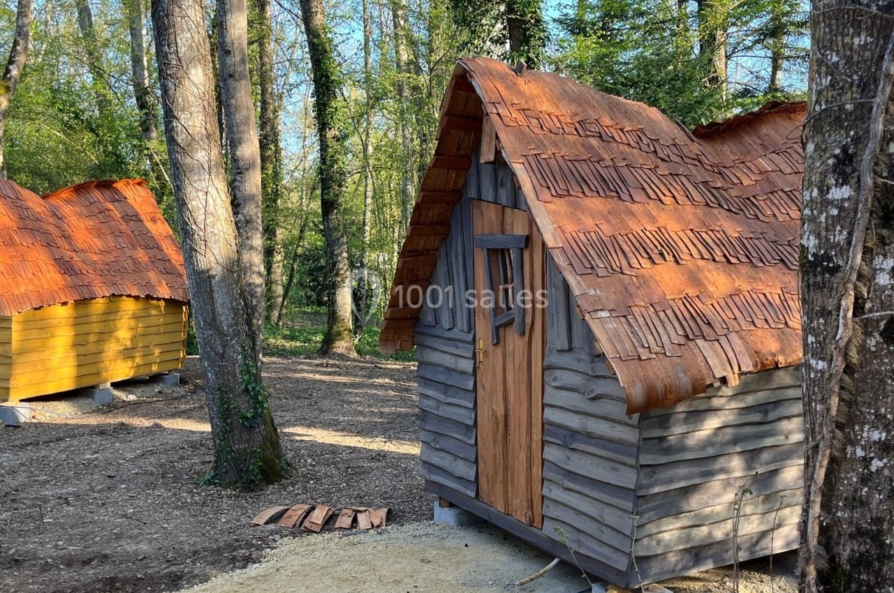 Petites cabanes en bois avec toits en tuiles dans une forêt, entourées d'arbres et de végétation.