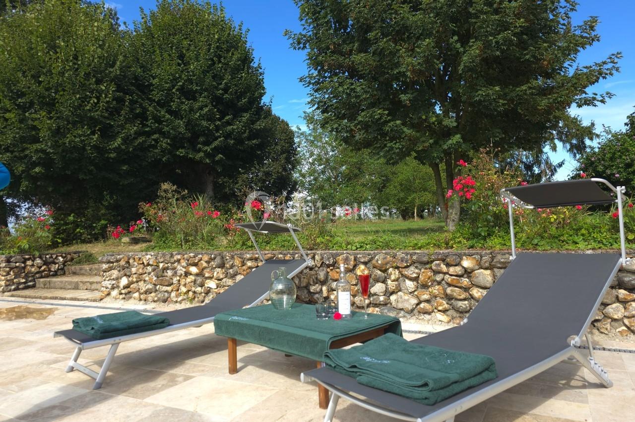 Deux transats gris avec serviettes vertes près d'une piscine, entourés de végétation et de fleurs.