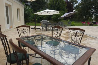 Tables dressées avec nappes blanches et décoration florale sur une terrasse ensoleillée, avec des convives en arrière-plan.