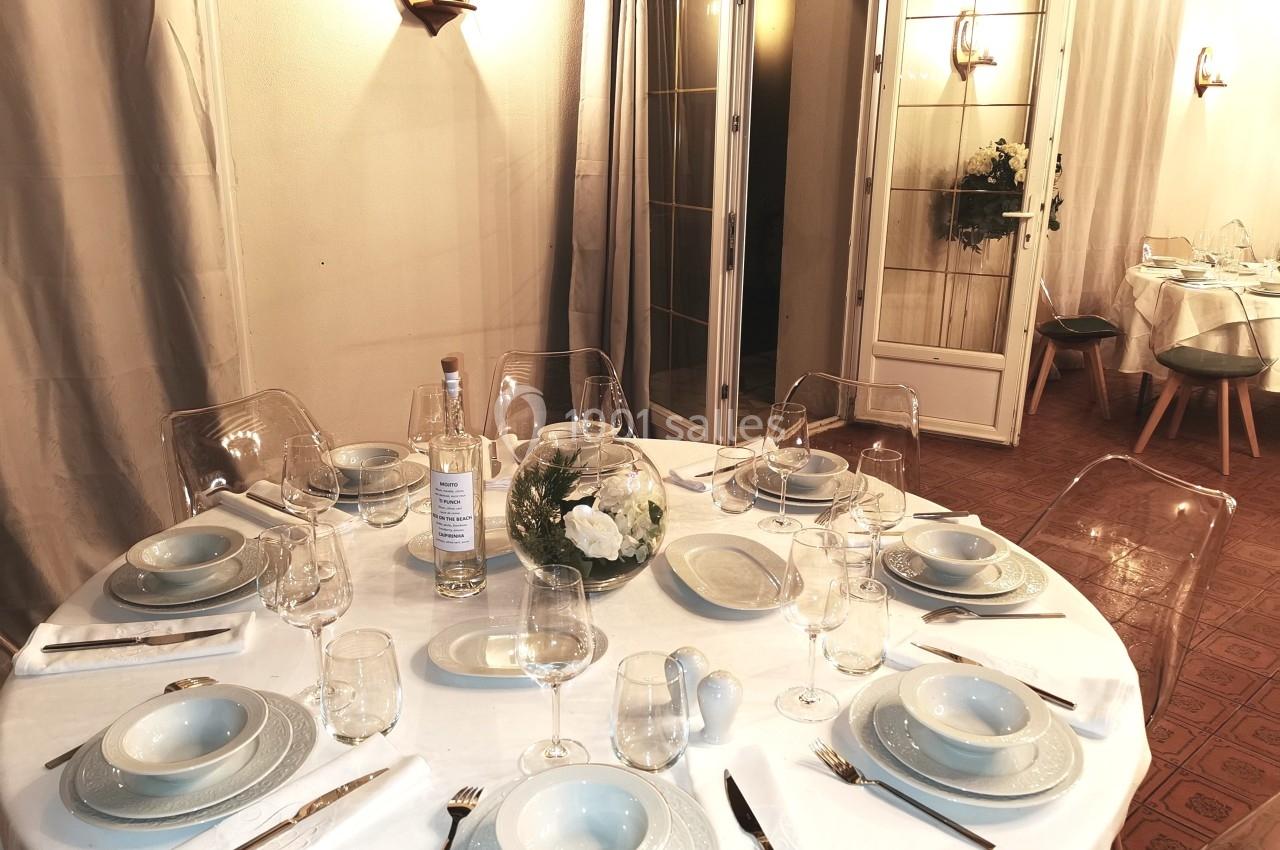 Table ronde dressée avec vaisselle blanche, verres, couverts et centre de table floral dans un espace intérieur chaleureux.