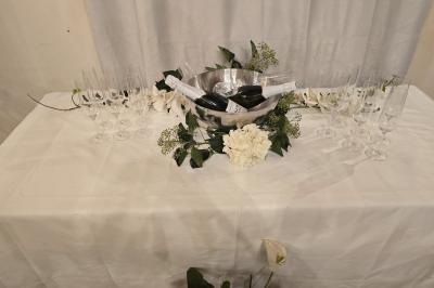 Tables dressées avec nappes blanches et décoration florale sur une terrasse ensoleillée, avec des convives en arrière-plan.