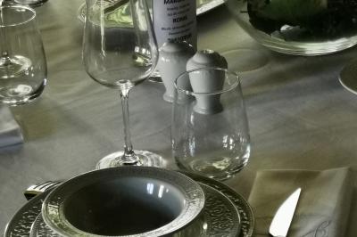 Tables dressées avec nappes blanches et décoration florale sur une terrasse ensoleillée, avec des convives en arrière-plan.