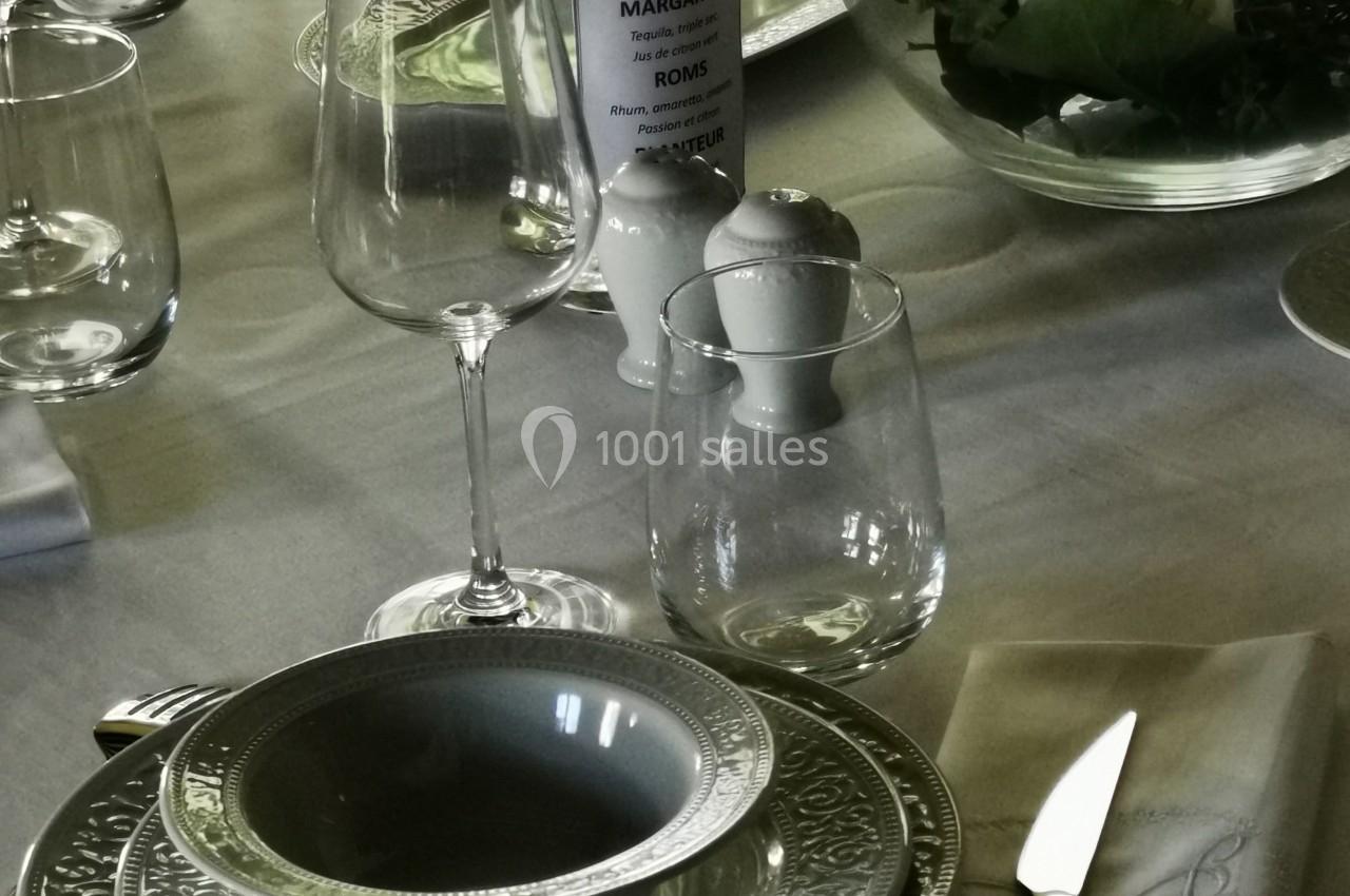 Table dressée avec vaisselle élégante, verres, serviette pliée et centre de table floral dans un bol en verre.