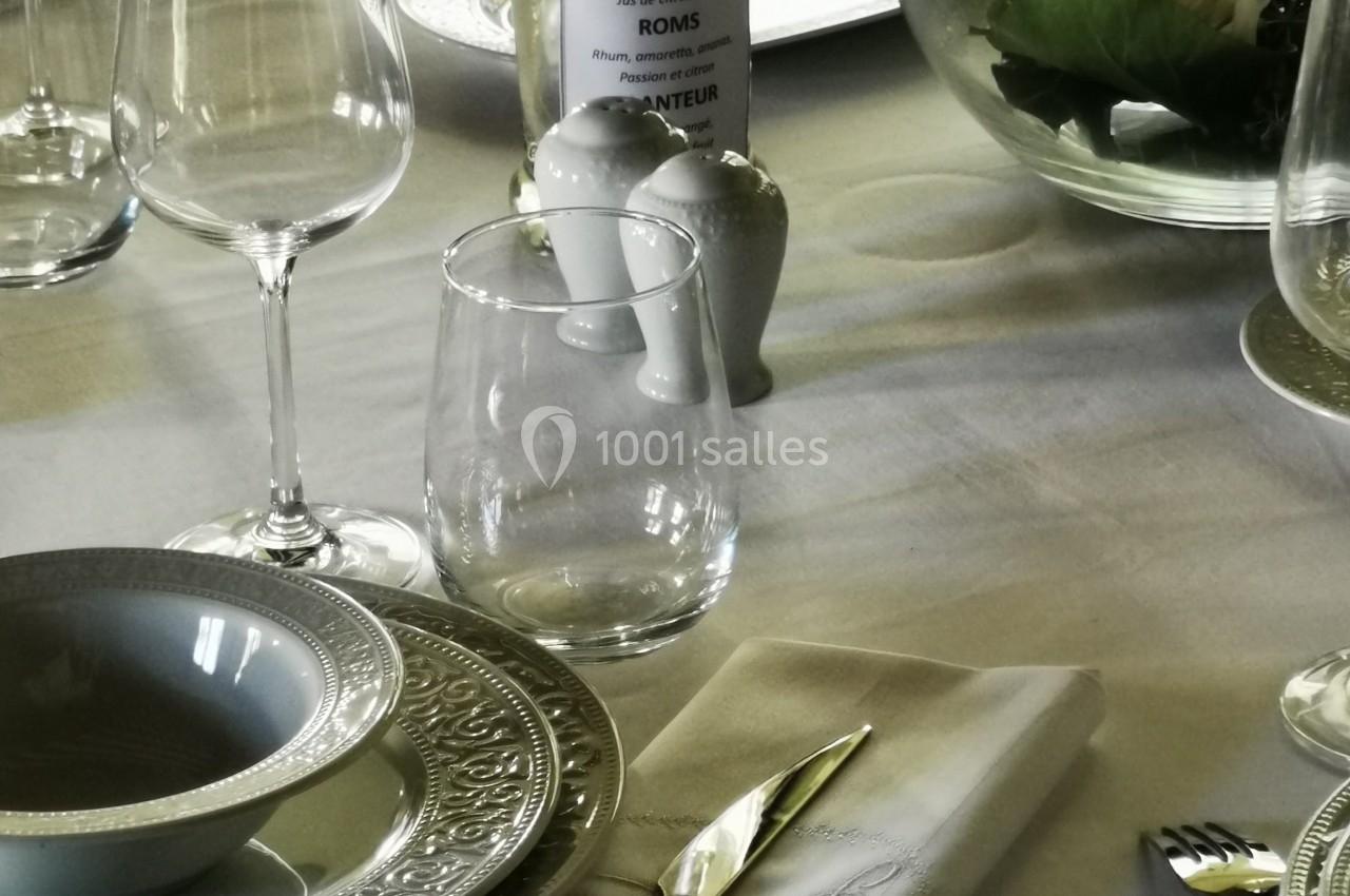 Table élégamment dressée avec vaisselle raffinée, serviette pliée, verres et centre de table floral.