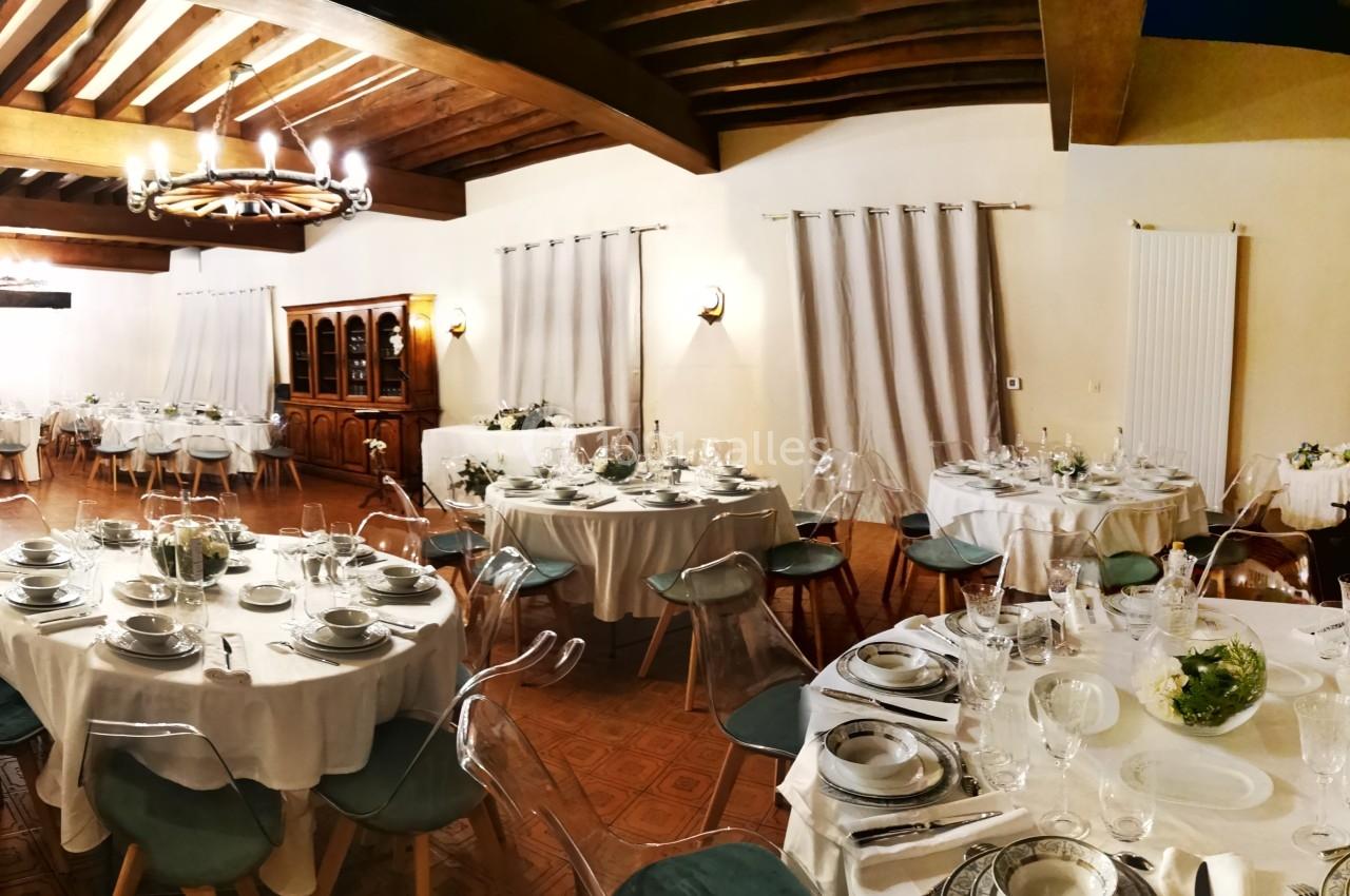 Salle de réception élégante avec tables rondes dressées, nappes blanches et décoration raffinée dans un cadre chaleureux.