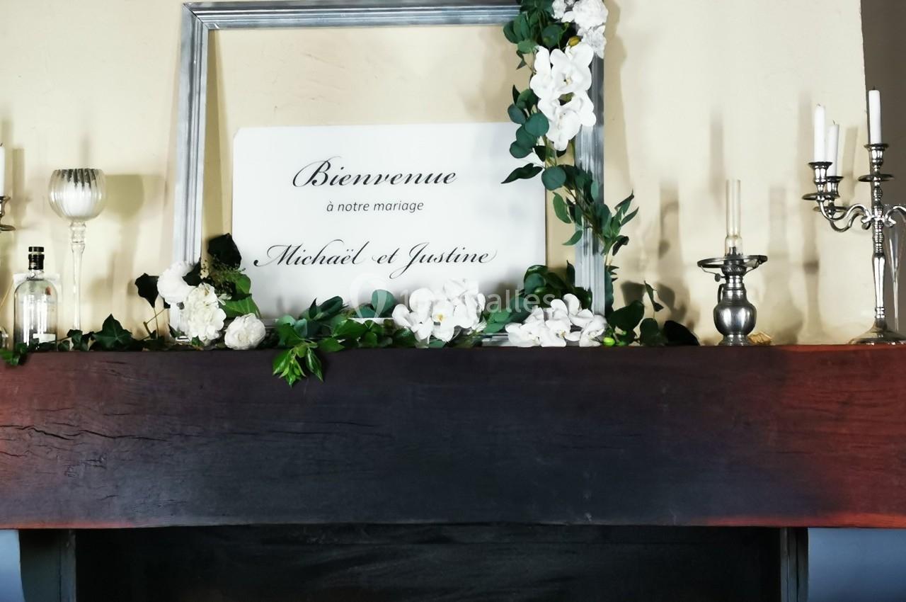 Cadre argenté avec un panneau ’Bienvenue à notre mariage Michael et Justine’, entouré de fleurs blanches et feuillage.