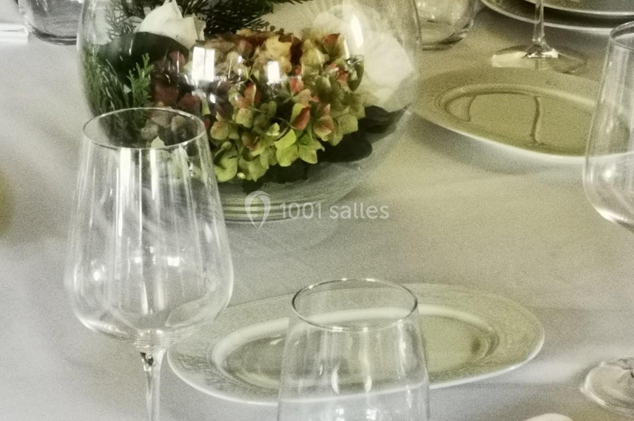 Table dressée avec vaisselle blanche, verres transparents et centre de table floral dans un vase rond en verre.