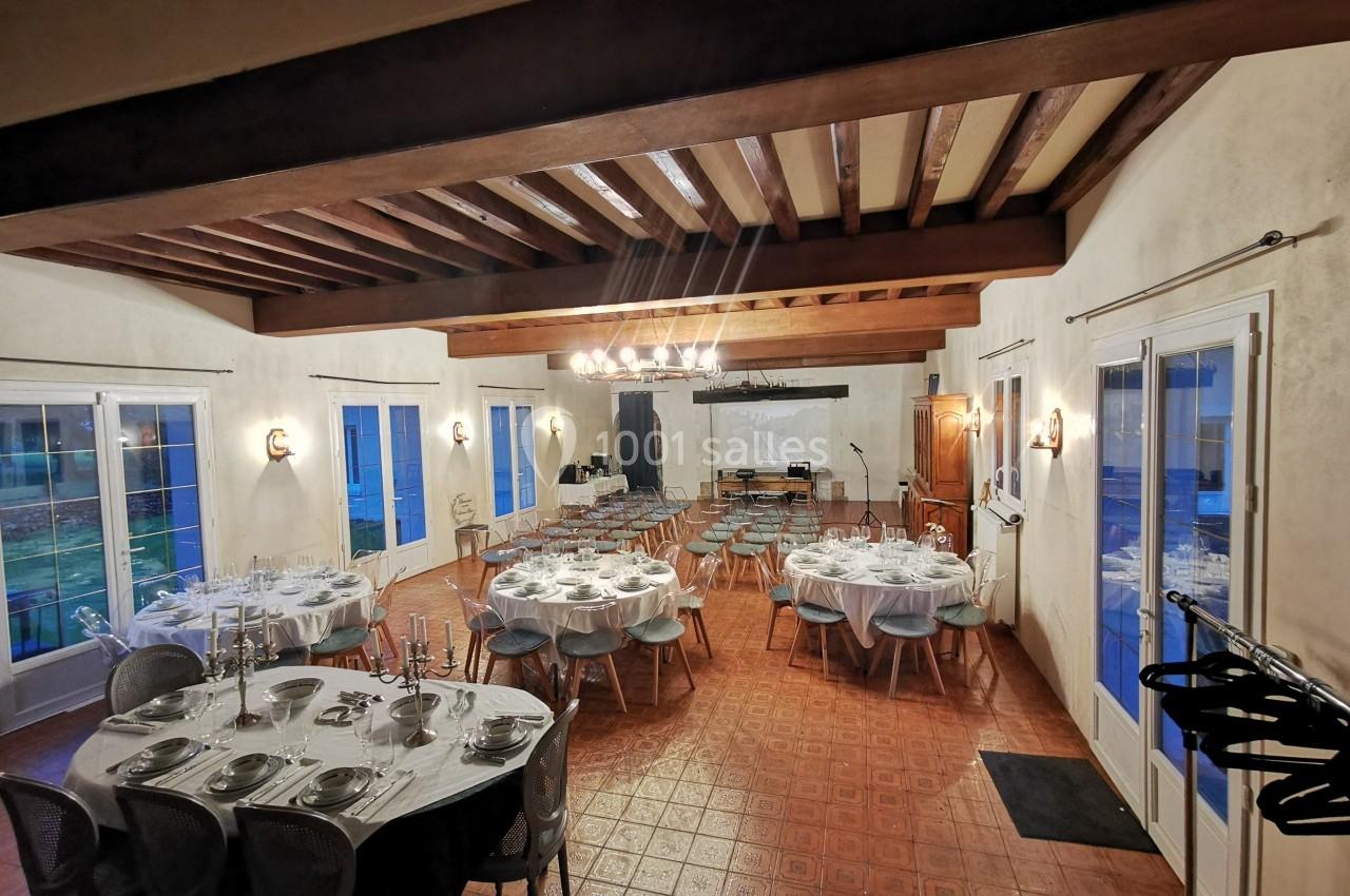 Salle de réception avec tables dressées pour un repas et chaises disposées face à un écran de projection.
