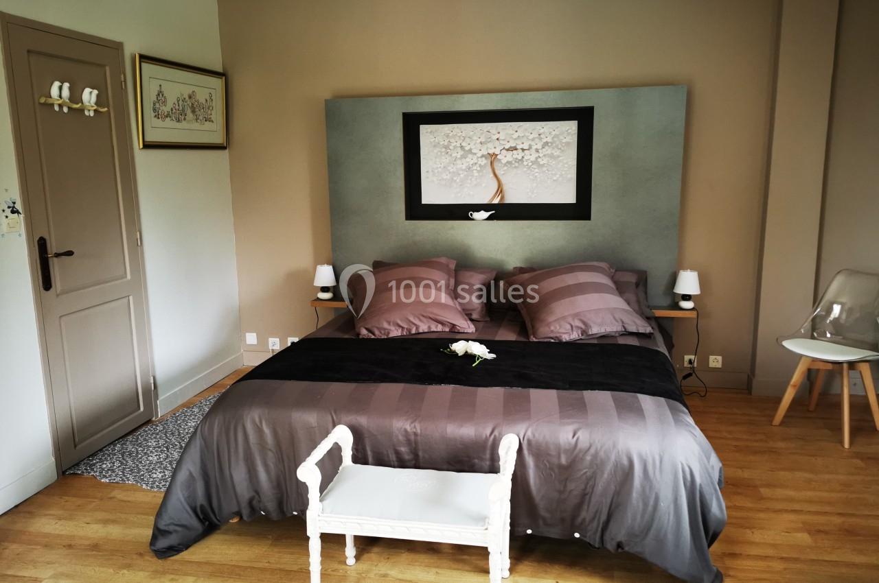 Chambre avec lit double, tête de lit décorée, murs beige et mobilier minimaliste sur parquet en bois clair.