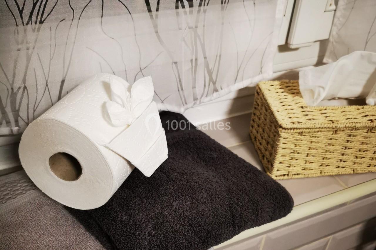 Rouleau de papier toilette posé sur une serviette noire près d'une boîte en osier contenant des mouchoirs.