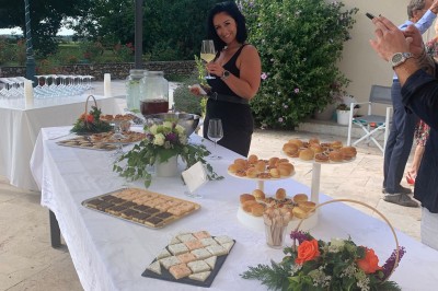 Tables dressées avec nappes blanches et décoration florale sur une terrasse ensoleillée, avec des convives en arrière-plan.