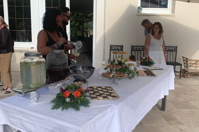 Tables dressées avec nappes blanches et décoration florale sur une terrasse ensoleillée, avec des convives en arrière-plan.