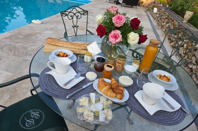 Tables dressées avec nappes blanches et décoration florale sur une terrasse ensoleillée, avec des convives en arrière-plan.