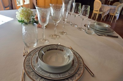 Tables dressées avec nappes blanches et décoration florale sur une terrasse ensoleillée, avec des convives en arrière-plan.