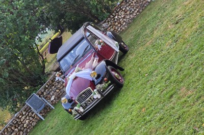 Tables dressées avec nappes blanches et décoration florale sur une terrasse ensoleillée, avec des convives en arrière-plan.