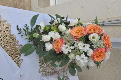Tables dressées avec nappes blanches et décoration florale sur une terrasse ensoleillée, avec des convives en arrière-plan.