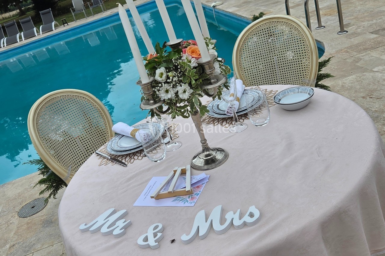 Table décorée pour un mariage avec chandelier, vaisselle élégante et inscription ’Mr & Mrs’, près d'une piscine.