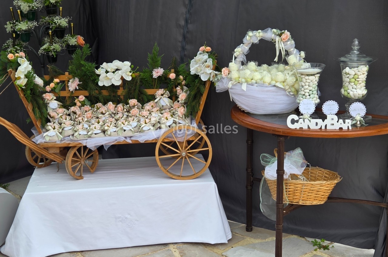 Chariot en bois décoré de fleurs et table avec bonbonnières remplies de dragées, disposés pour une réception.