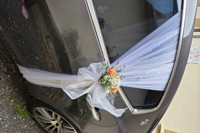 Tables dressées avec nappes blanches et décoration florale sur une terrasse ensoleillée, avec des convives en arrière-plan.