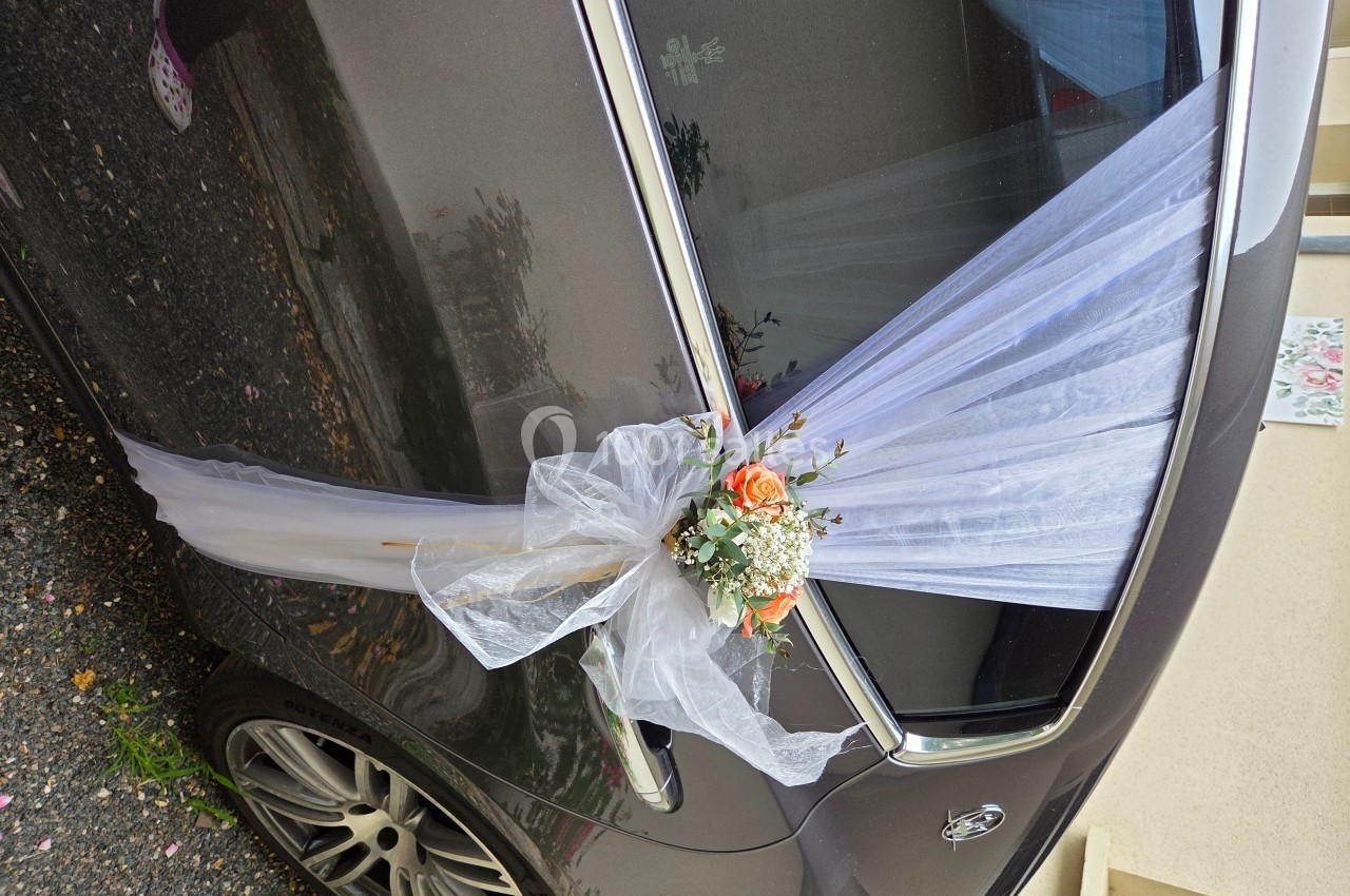 Voiture décorée pour un mariage avec un voile blanc et un bouquet de fleurs roses et blanches fixé sur la portière.