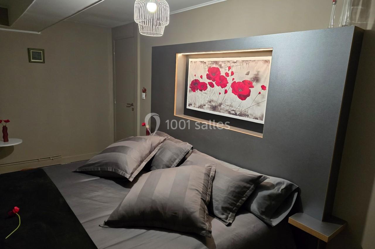 Lit double avec draps gris, tableau de coquelicots rouges au mur, éclairage doux et décoration minimaliste.