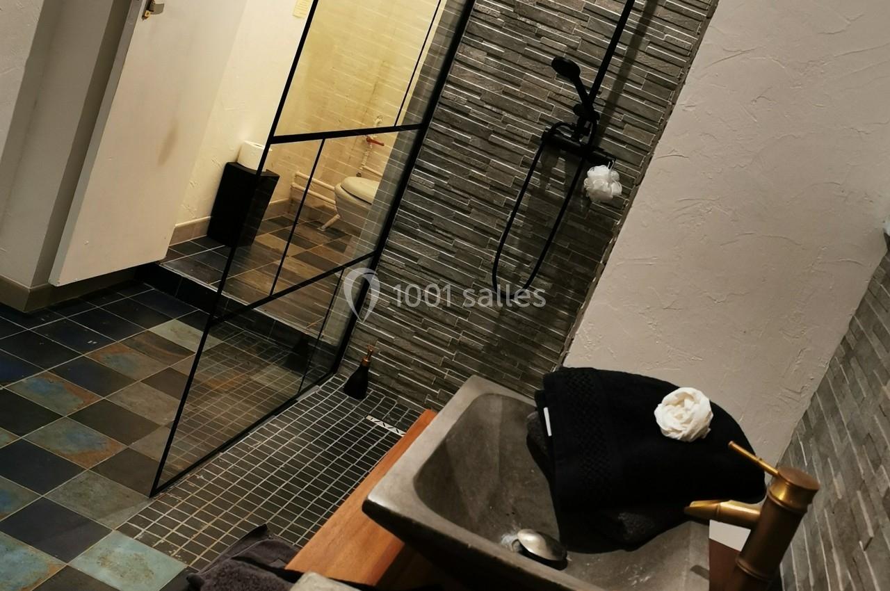 Salle de bain moderne avec douche à paroi vitrée, double vasque en pierre et robinetterie dorée.