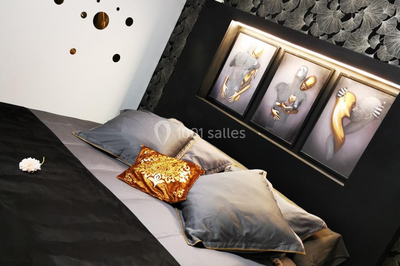 Lit double avec linge de lit gris et noir, décor mural floral sombre, tableaux modernes et coussin doré.