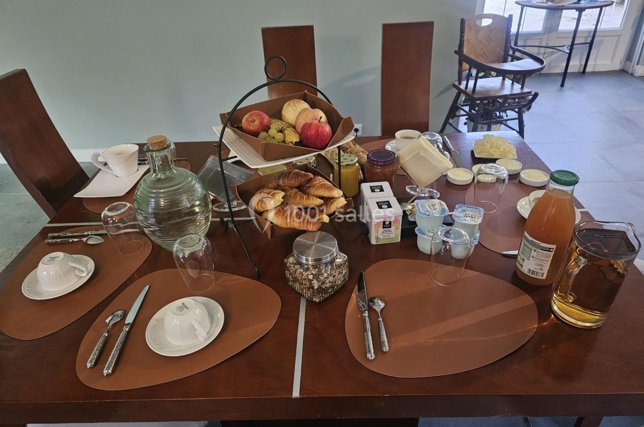 Table dressée pour un petit-déjeuner avec viennoiseries, fruits, boissons, yaourts et condiments variés.