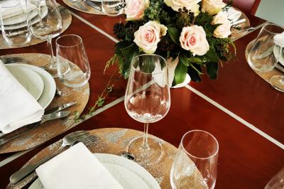 Tables dressées avec nappes blanches et décoration florale sur une terrasse ensoleillée, avec des convives en arrière-plan.