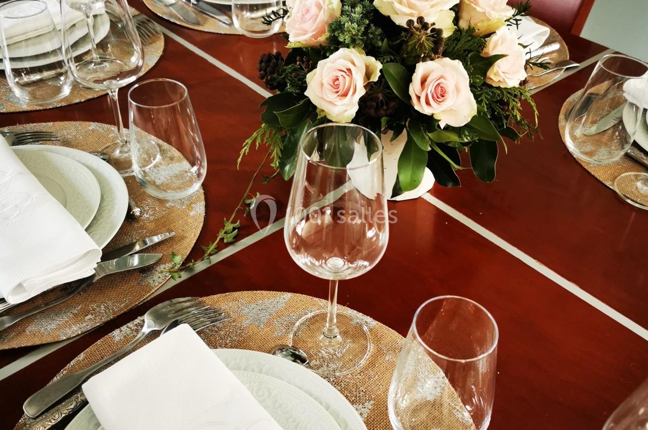 Table dressée avec des assiettes blanches, serviettes pliées, verres et un bouquet de roses au centre.