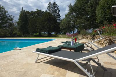 Piscine extérieure bordée de dalles, devant une grande maison traditionnelle avec toit en tuiles rouges.