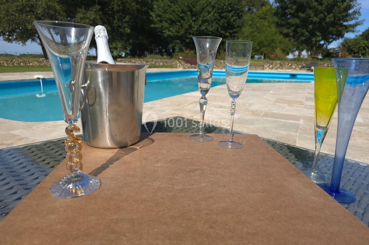 Seau à champagne, flûtes en verre et piscine en arrière-plan sur une terrasse ensoleillée.