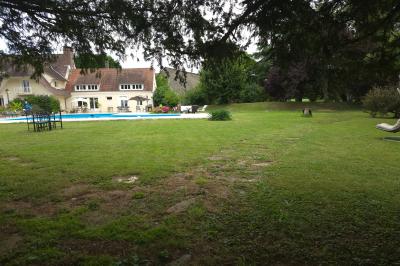 Piscine extérieure bordée de dalles, devant une grande maison traditionnelle avec toit en tuiles rouges.