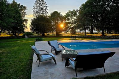 Piscine extérieure bordée de dalles, devant une grande maison traditionnelle avec toit en tuiles rouges.