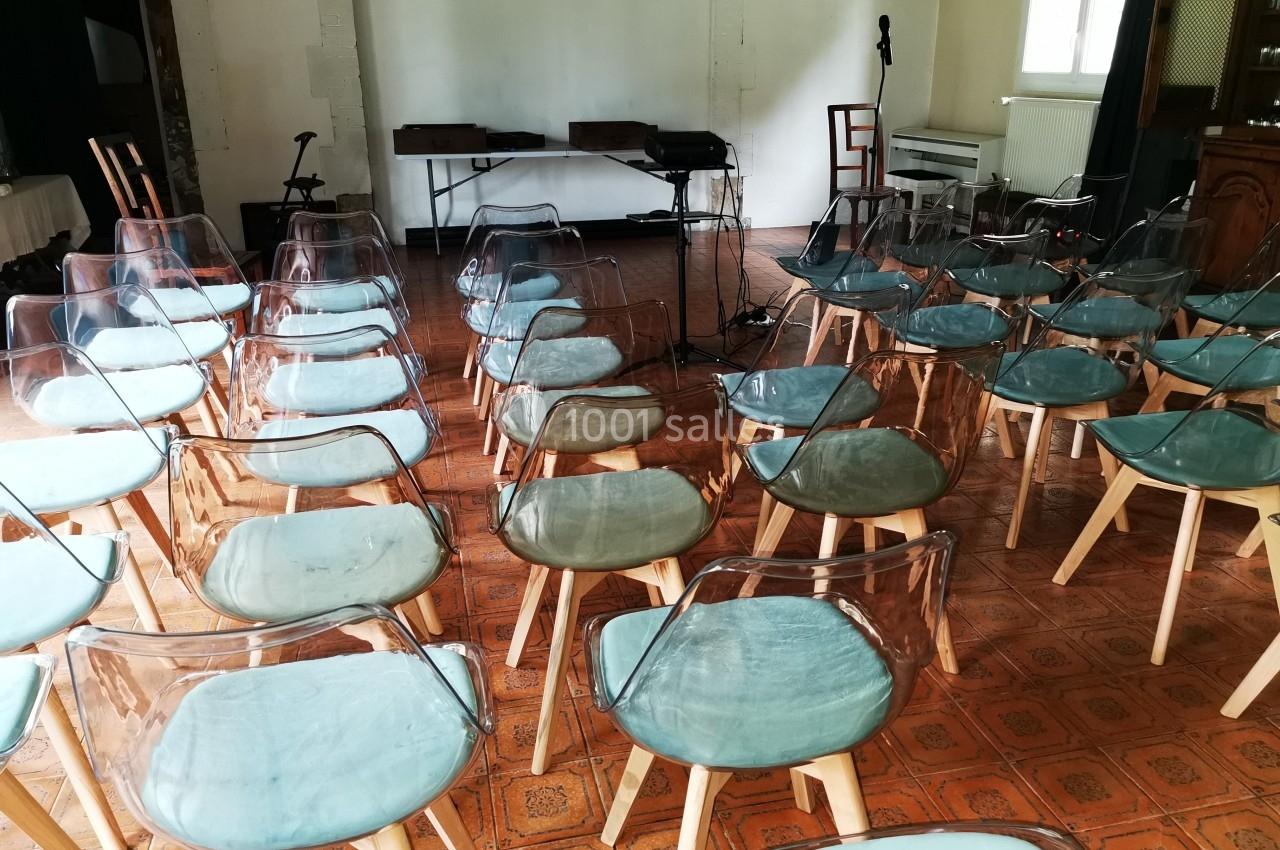 Chaises transparentes disposées en rangées dans une salle avec un sol en carrelage, face à un espace équipé de micros.