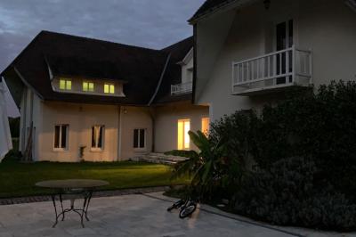 Piscine extérieure bordée de dalles, devant une grande maison traditionnelle avec toit en tuiles rouges.