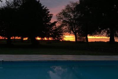 Piscine extérieure bordée de dalles, devant une grande maison traditionnelle avec toit en tuiles rouges.