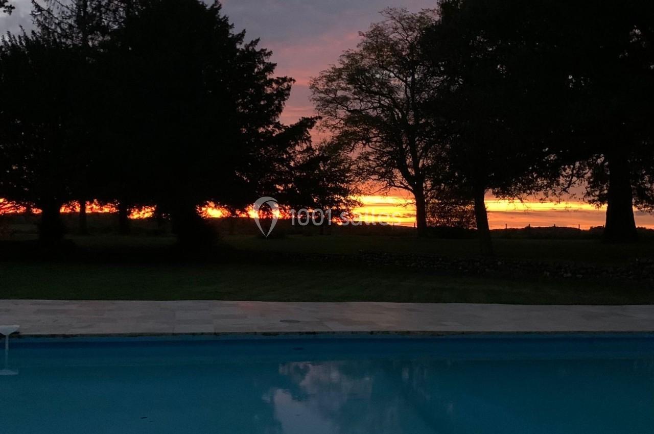 Piscine extérieure reflétant un ciel au coucher du soleil avec des arbres en silhouette à l'arrière-plan.