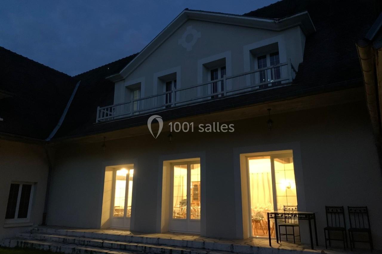 Façade d'une maison éclairée de nuit, avec des fenêtres et une porte-fenêtre donnant sur une terrasse.