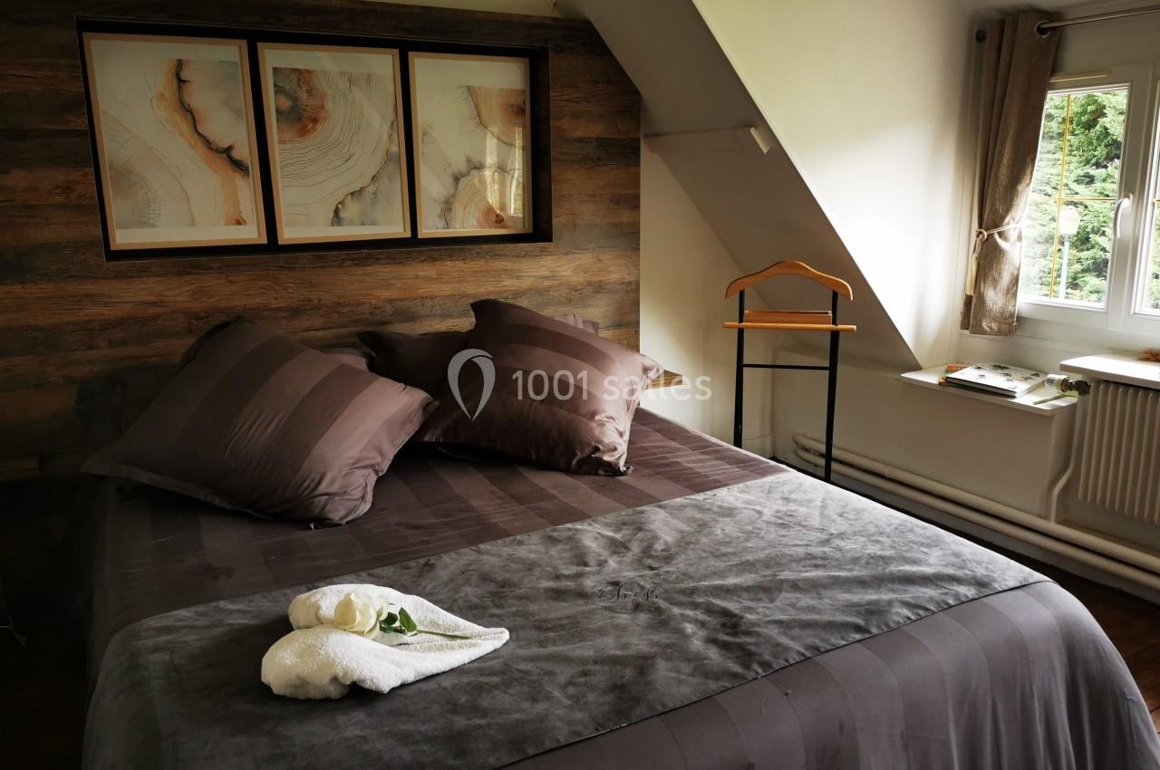 Lit double avec draps et coussins marron, serviettes pliées en forme de cygne, fenêtre donnant sur un jardin verdoyant.