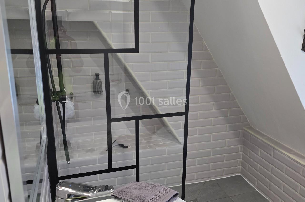 Salle de bain moderne avec douche à l'italienne, paroi vitrée à cadre noir, lavabo et carrelage blanc.