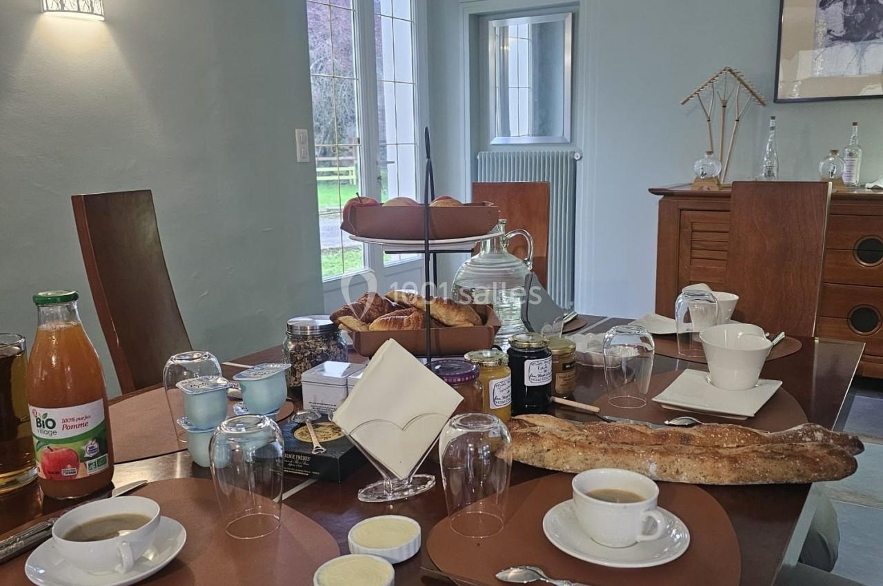 Table dressée pour un petit-déjeuner avec pain, viennoiseries, confitures, jus de fruit, café et vaisselle.