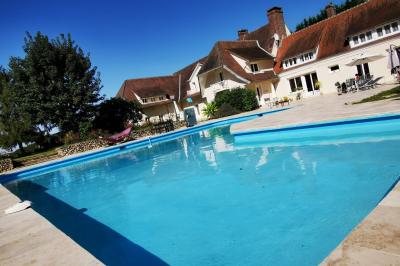 Piscine extérieure bordée de dalles, devant une grande maison traditionnelle avec toit en tuiles rouges.