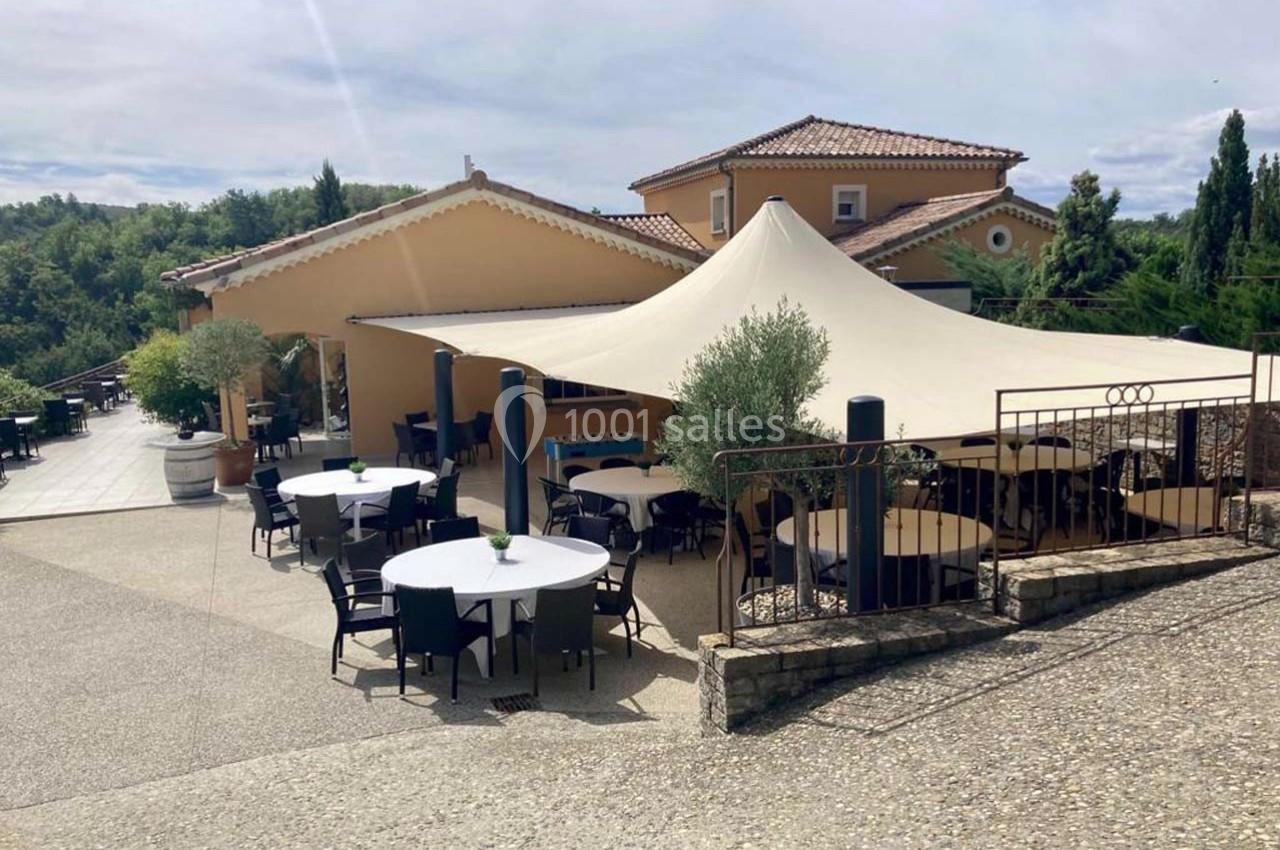 Terrasse extérieure d'un restaurant avec tables et chaises sous une grande toile tendue, entourée de verdure.