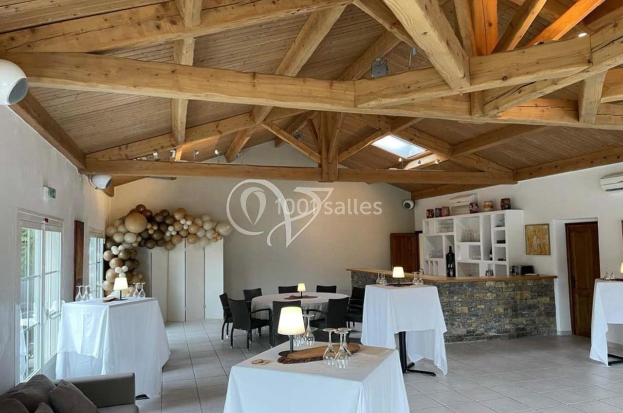 Salle lumineuse avec charpente en bois apparente, tables hautes dressées et décoration murale en ballons.