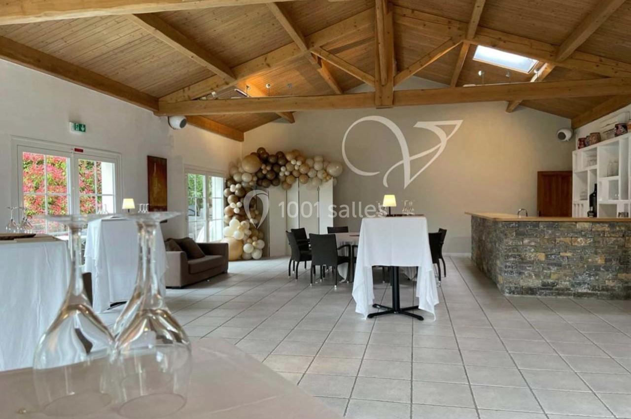 Salle lumineuse avec poutres apparentes, tables dressées, décoration de ballons et bar en pierre.