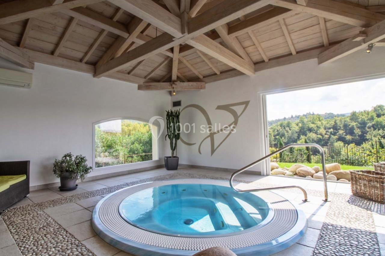 Bain à remous intérieur entouré de plantes, avec vue sur un paysage verdoyant à travers de grandes ouvertures.