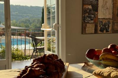 Vue d'une table avec croissants et fruits, devant une porte ouverte sur une terrasse avec piscine et paysage verdoyant.