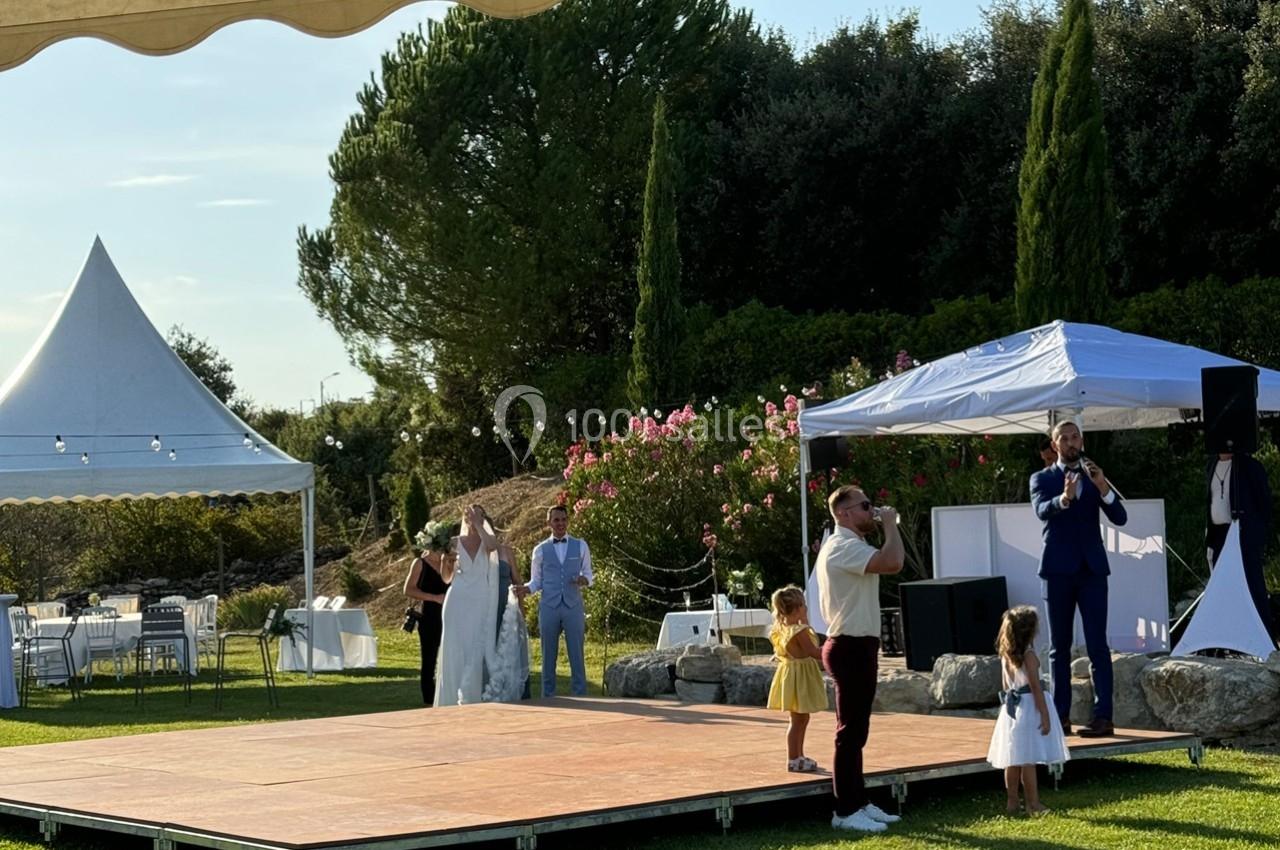 Un couple de mariés et des invités sur une piste de danse en extérieur, entourés de tentes et de végétation.